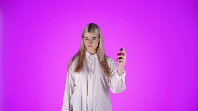 Blond kobieta w białej koszuli i okularach perfumująca nadgarstek i wąchająca zapach z uśmiechem &mdash; fioletowe tło, styl, kobiecość i elegancja w slow motion 4K