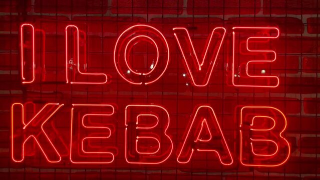 Neon glowing red sign on a brick wall with the inscription or slogan I love kebab. Brick wall, background. Bright electric neon light. Cafe-restaurant Doner Kebab.