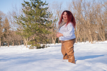 A fat red-haired woman in a white sweatshirt walks through snowdrifts. 