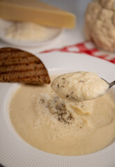 Cauliflower cream soup served in an elegant white plate with wide side, accompanied by a piece of grilled bread on the side. recipe for vegan vegetable soup