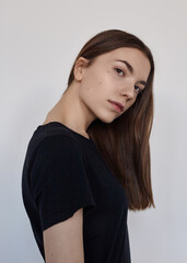 A cute woman in a black T-shirt poses on a light background
