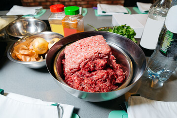 Ground Beef Preparation for Cooking. A stainless steel bowl filled with fresh ground beef ready for culinary preparations, surrounded by various cooking ingredients.