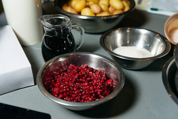 Bowl of Fresh Red Currants in Kitchen Setting. A stainless steel bowl filled with vibrant red currants on a kitchen countertop, surrounded by cooking ingredients.