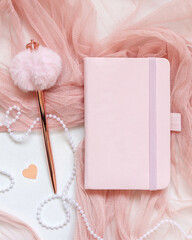 Pink hardcover notebook near hearts, pen, tulle and vase on white table top view, textbook mockup