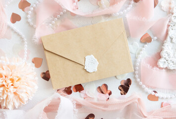 Envelope near pink decorations, hearts and silk ribbons on white table top view, mockup