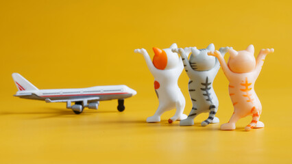 Three toy kittens with raised legs and passenger airplane on yellow background. Concept of greeting...