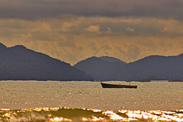 boat anchored near the surf, on a golden ocean reflecting the twilight light, in the background the...