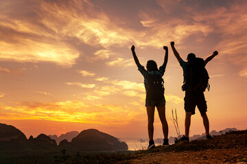 Happy young couple of hikers with backpacks are standing with open arms at sunrise viewpoint. Phang Nga province, Thailand