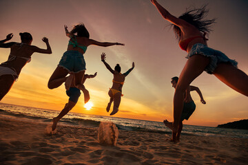 Big group of happy young friends are having fun and jumps at sunset sea beach. Silhouettes of...