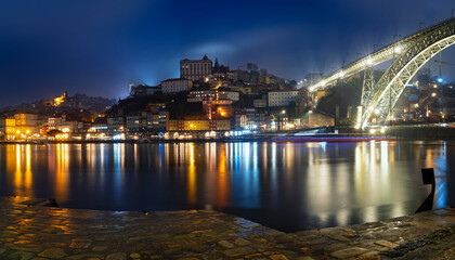 Fototapeta na wymiar Panoramic long exposure night view of Porto, Portugal, the Douro River, and Dom Luis Bridge during a rainy night