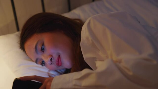 Asian couple sleeping in bed. Cheating wife. Couple issue. Infidelity betrayal. Disloyal woman using mobile phone for chatting to lover  lying in bed with sleeping husband late at night in warm light.