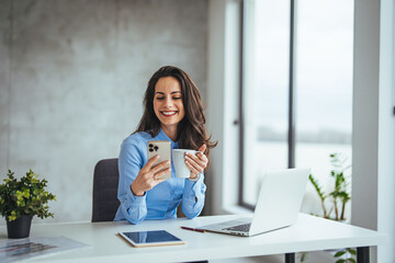 Shot of a young businesswoman using a mobile phone and laptop at her desk in a modern office....