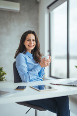 An attractive young businesswoman having coffee while working at her office desk. Laughing young ...