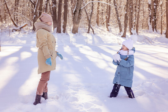 Two sisters in warm winter clothes have fun and play with a snow in winter in the forest. Winter activities concept image. Happy family time