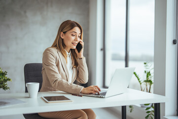 Business woman working and talking on a mobile phone. She is sitting at a table with a laptop...