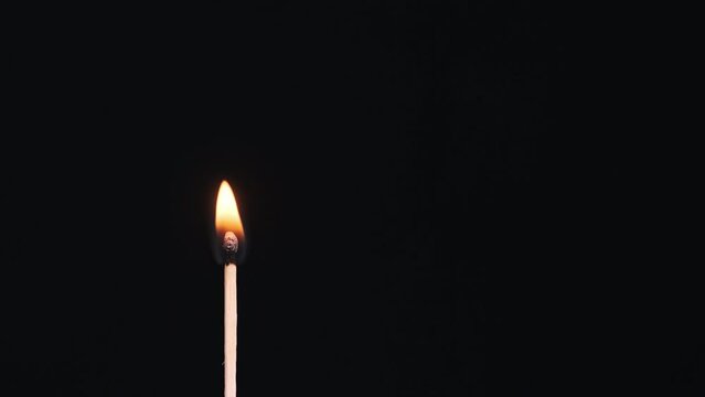 The match stick ignites and burns on a black background close-up, copy space. Igniting match sulfur. One match stick magically lighting and lit. Fire flame from matchstick. 4K, 59,94fps.