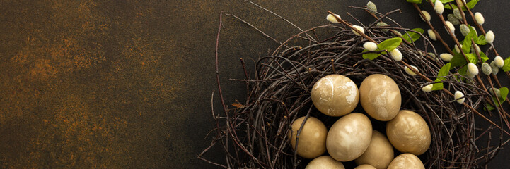 Colorful Easter eggs in a nest with willow branches on a brown background, top view, copy space, Easter banner