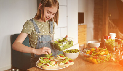 Girl preparing sandwiches with avocado, tomatoes cherry and arugula at kitchen. Vegetarian bruschettas and salad with fresh vegetables and greens