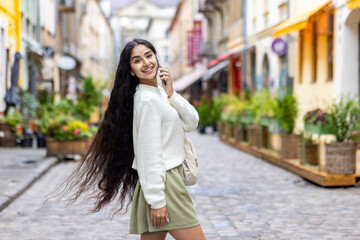 Portrait of a beautiful young Indian woman with long hair walking on a city street, talking on the phone, posing and looking at the camera