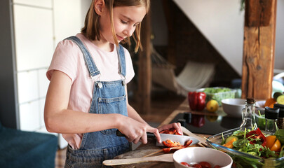 Cute Little Girl Cooking A Vegetable Salad In The Kitchen, Cutting Red Paprika On A Cutting Board