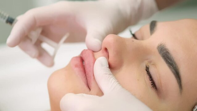Beauty injections. Lip augmentation procedure. Lip injection. A cosmetologist in medical gloves gives a beauty injection to a young client in a medical cabin.