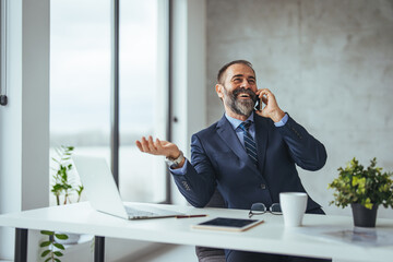 Man working at his desk at office. Smiling mature businessman holding smartphone sitting in office....