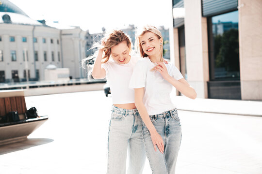Two young beautiful smiling hipster female in trendy summer white t-shirt and jeans clothes. Carefree women posing in the street. Positive models having fun outdoors. Cheerful and happy