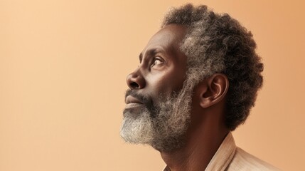 A contemplative man with a gray beard and curly hair looking upwards with a thoughtful expression set against a soft warm-toned background.