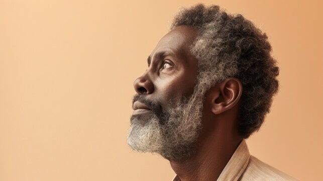 A contemplative man with a gray beard and curly hair looking upwards with a thoughtful expression set against a soft warm-toned background.