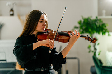 A young elegant girl rehearses the melody of a classical piece of music on the violin in a bright...