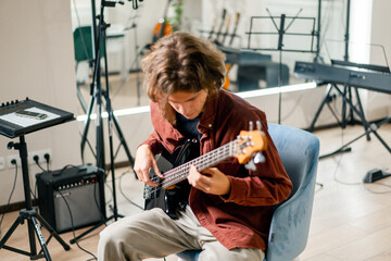 rock artist with long hair with electric guitar in recording studio playing own track musical...