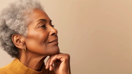 A contemplative woman with gray hair wearing a gold earring resting her chin on her hand against a neutral background. - obrazy, fototapety, plakaty