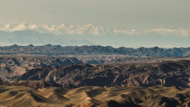 Mountainous terrain with beautiful skin rocky slopes with snow peaks background. Martian plateau landscape in Kazakhstan at summer sunny sunset.