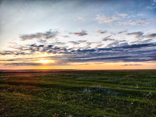 Sunset with the sun and a dramatic cloud over steppe with green grass. Beautiful nature landscape