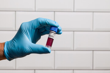 Close-up of doctor's hand wearing blue medical gloves holding a blood probe in front of a laboratory wall