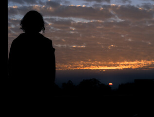 Fototapeta premium January 7th 2021. Dehradun Uttarakhand India. A Silhouette of a man with long hairs looking at the sun during sunset.