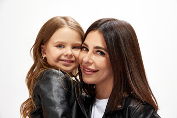 Beautiful happy young woman, mother embracing with little daughter, posing in same style outfit against white studio background. Concept of happiness, Mother's day, childhood, fashion and lifestyle