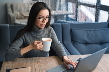 Portrait of attractive business woman with cup of coffee in her hand that working on her laptop at...