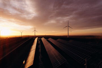 Solar panels park and wind turbines at sunset.Windmill turbines generating green energy electric.Green energy reduce carbon emissions and makes earth cleaner and more ecological.
