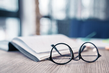 Eyeglasses at the wooden table with notebook on the background. Focus on glasses. Literature,...