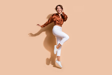 Fototapeta na wymiar Full length photo of shiny impressed woman wear brown blouse jumping high empty space isolated beige color background