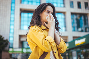 Woman with allergy symptom blowing nose. Outdoor shot of displeased Caucasian woman feels allergy,...