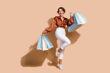Full length photo of pretty excited woman wear brown blouse rising bargains isolated beige color...