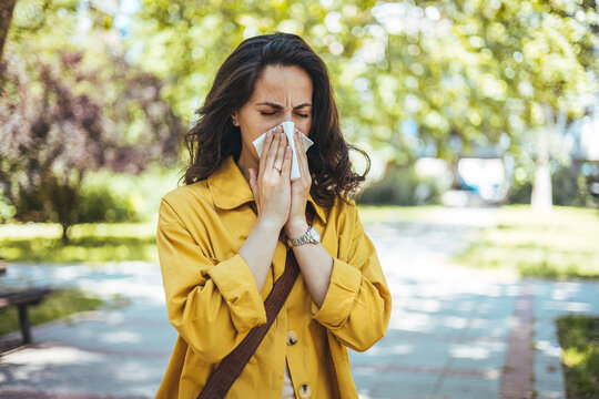 Woman struggling with allergy. Itchy eyes and sneezing. Attractive young adult woman coughing and sneezing outdoors. Sick people allergy or virus influenca concept.