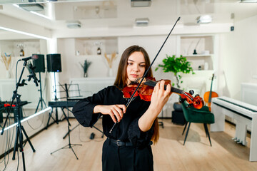 A young violinist plays with a bow on the strings of her violin against the background of musical...