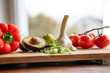 Healthy vegetables and fresh ingredients on wooden cutting board in front of bright kitchen window....