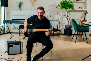 smiling rock artist with electric guitar in recording studio playing musical instrument during...
