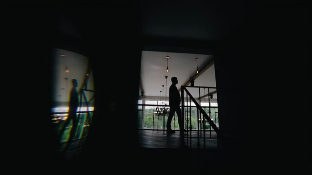 A man walks down a dark corridor. His silhouette is visible against the background of the light and the room