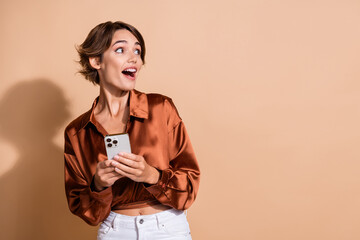 Photo of dreamy exited girl wear brown blouse communicating modern gadget looking empty space isolated beige color background