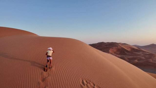 Aerial view of an adventure woman conquering Empty Quarter dunes in Oman, a solitary ascent against golden sands. Girl climbing the Rub' al-Khali desert dunes at sunset.